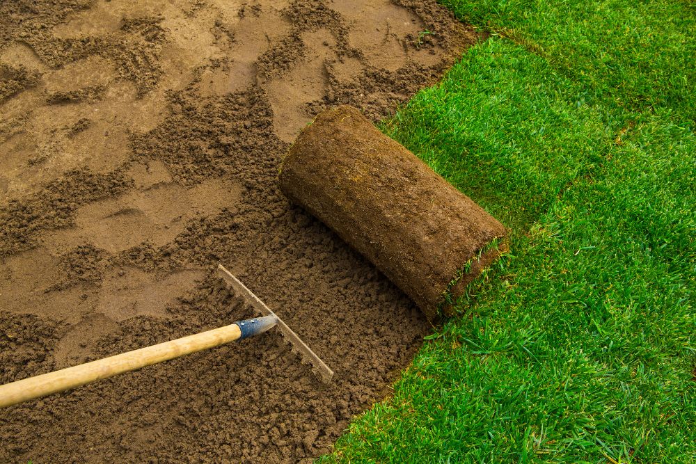 A lawn mower is positioned on the ground, with dirt being spread out beneath it.