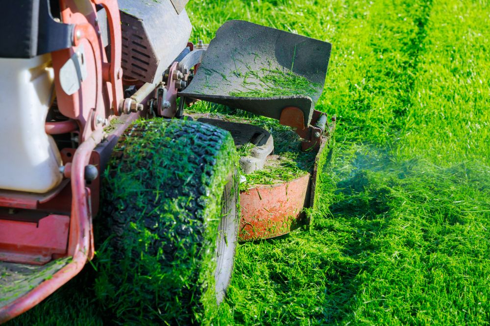 A lawn mower cutting grass in a green field under a clear blue sky.