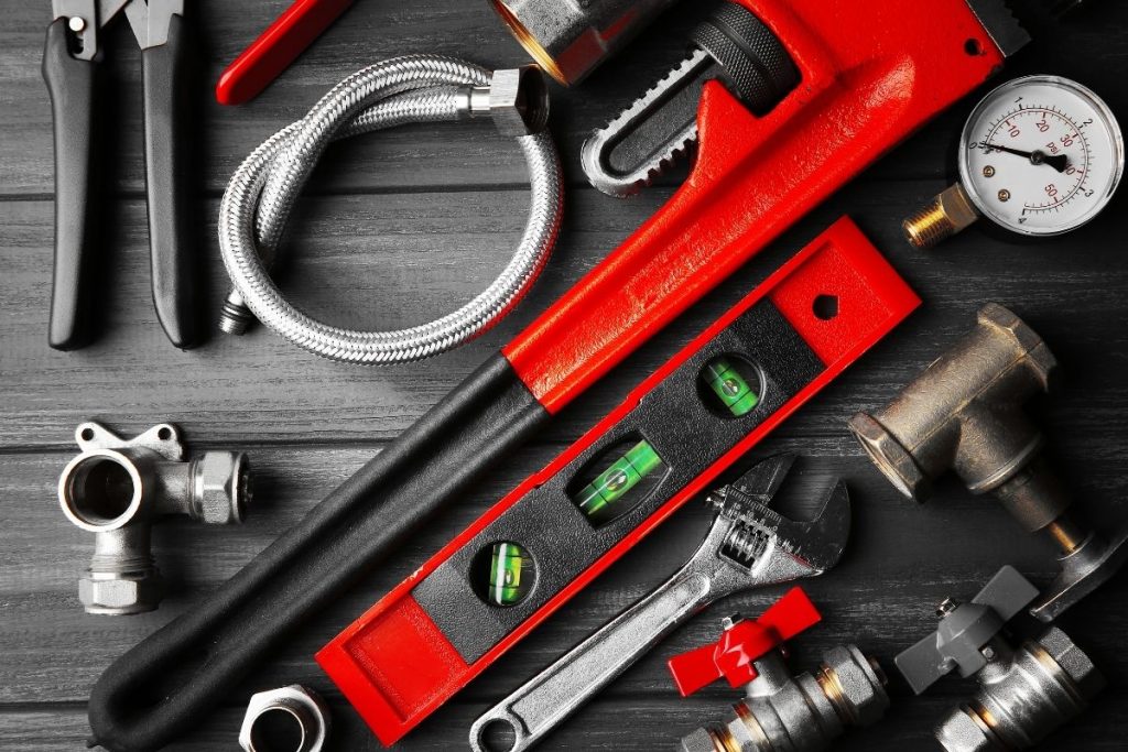 An assortment of plumbing tools and supplies arranged on a wooden table, featuring wrenches, pipes, and connectors.