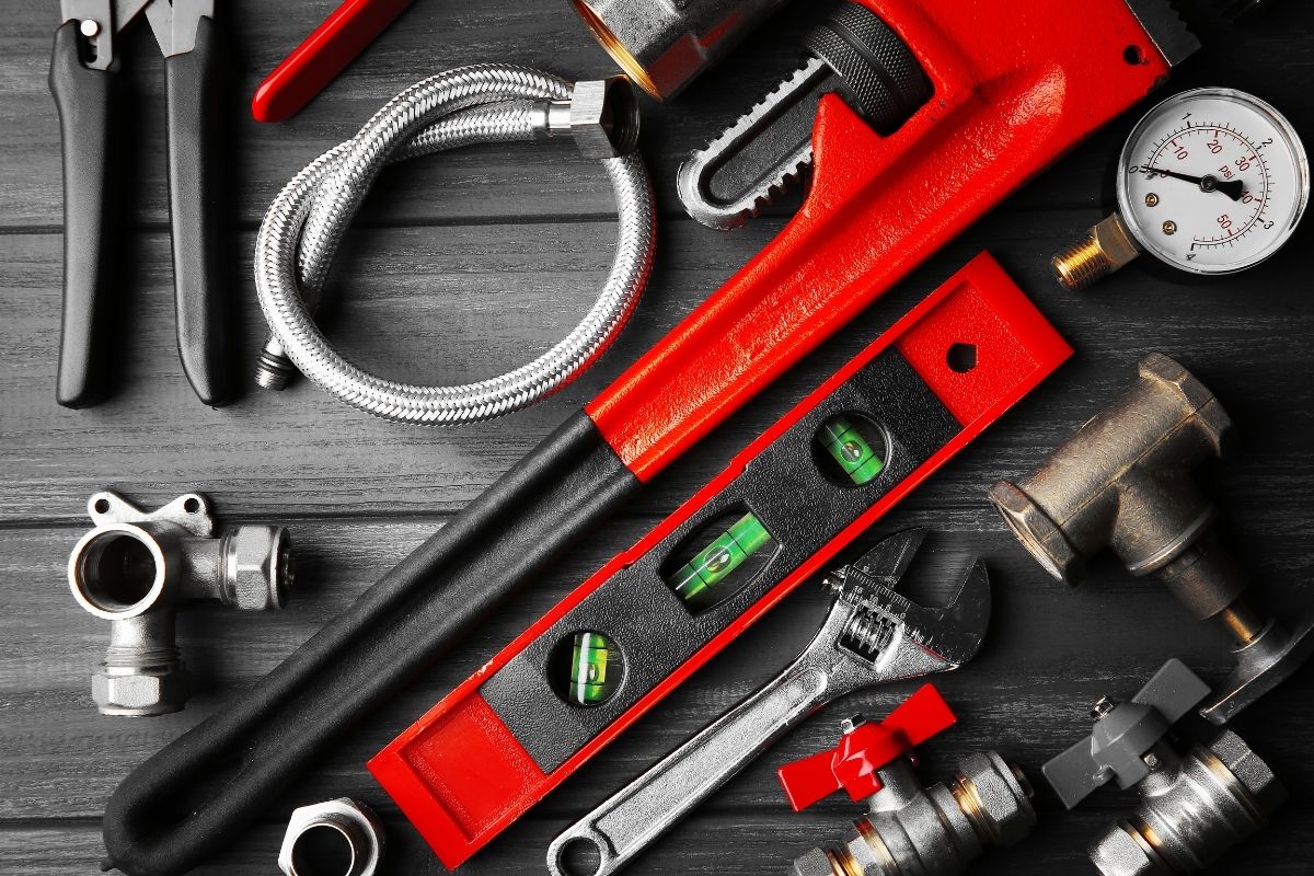 An assortment of plumbing tools and supplies arranged on a wooden table, featuring wrenches, pipes, and connectors.
